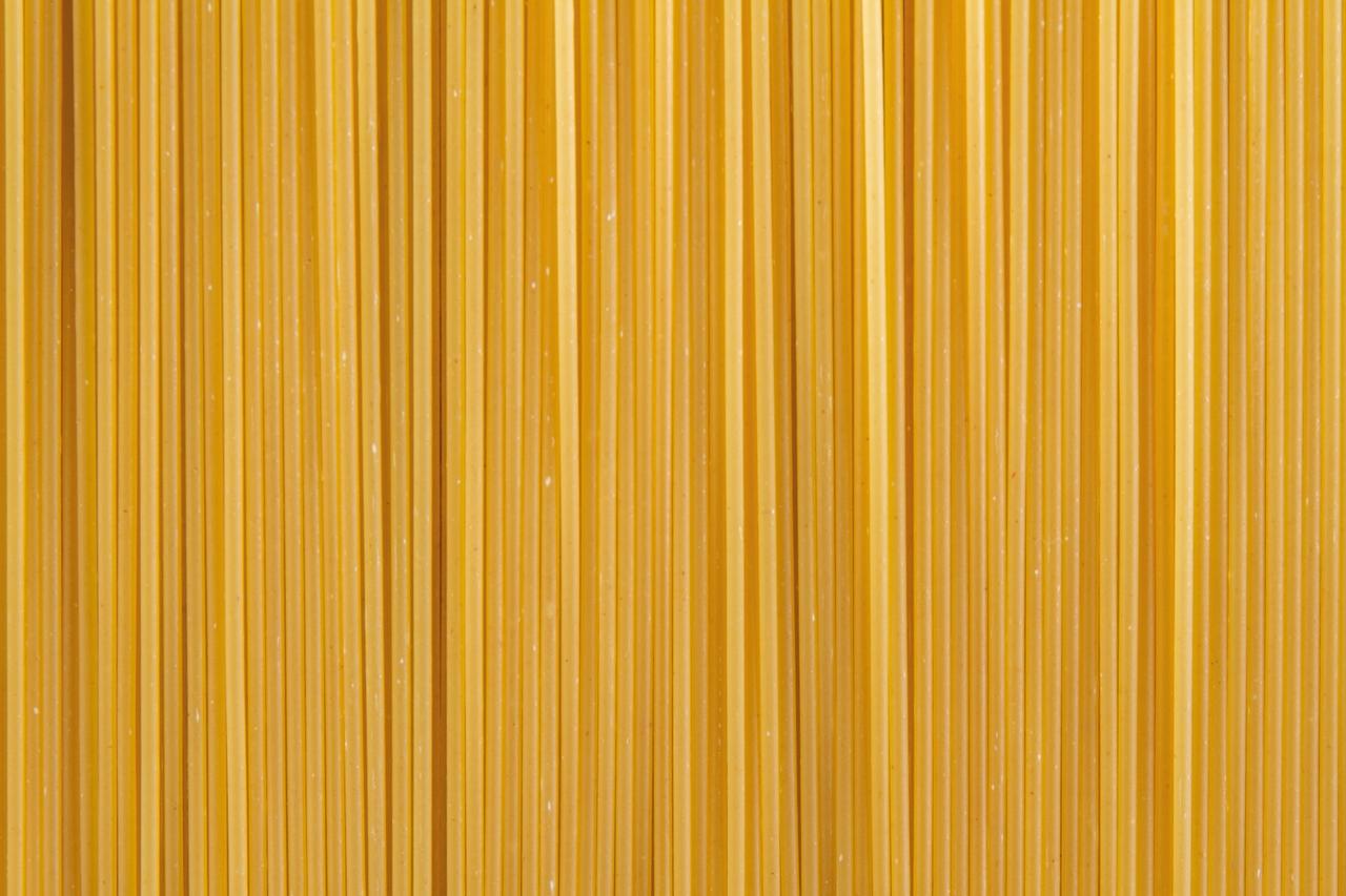 Detailaufnahme von vielen ungekochten Spaghetti, symmetrisch nebeneinander ausgebreitet.